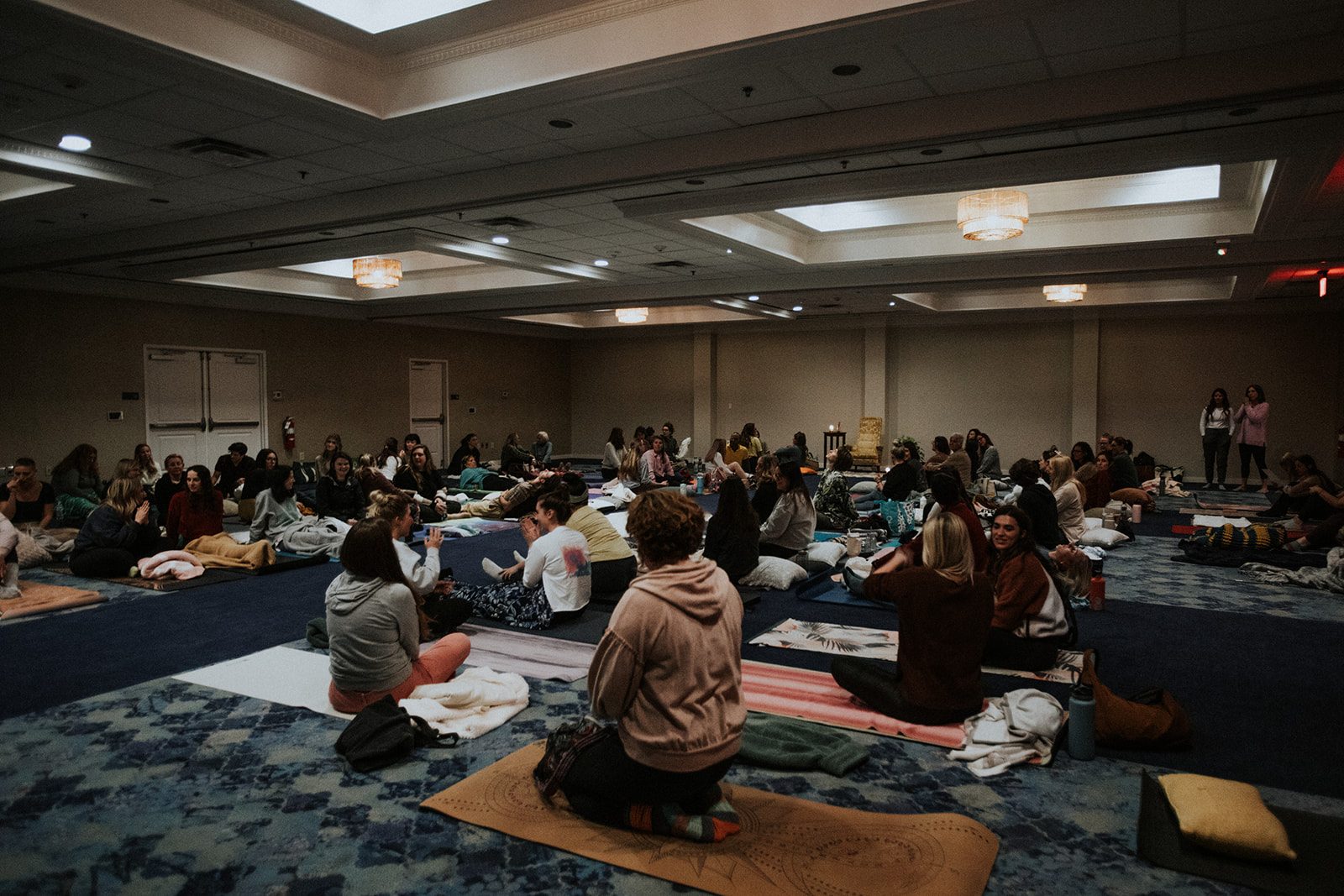Full wide view of a past gathering, room full of people on mats and cushions